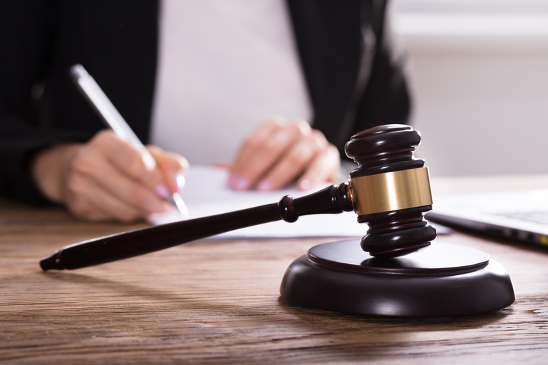 En domarklubba ligger på ett skrivbord medan en person skriver på papper i bakgrunden.