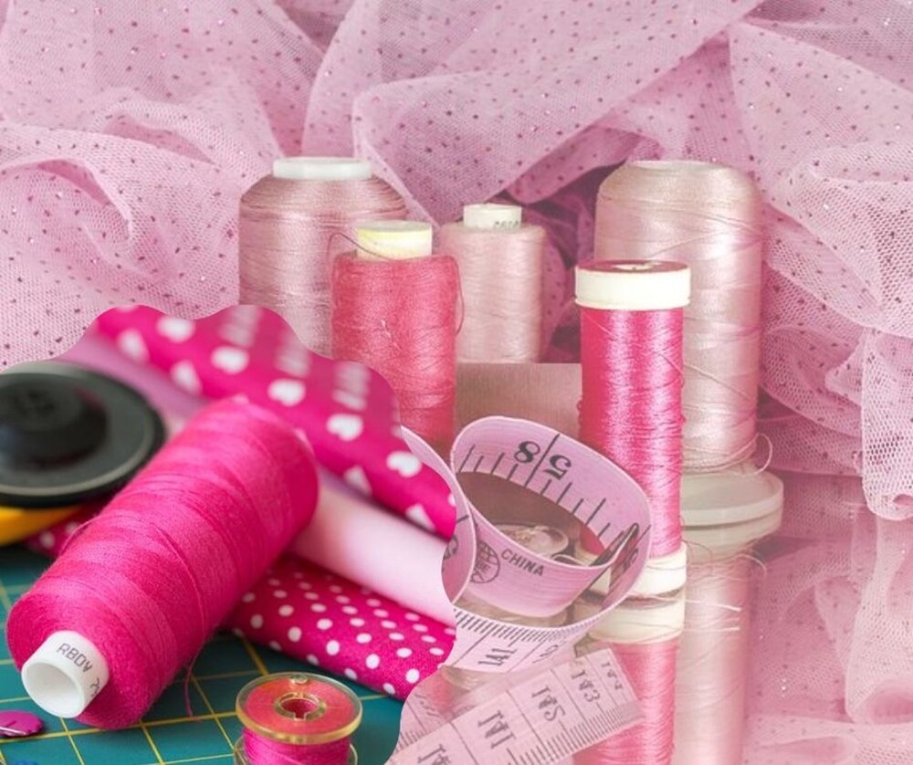 Flera rullar rosa sytråd, måttband, tyg och en rullkniv på ett bord med rosa tyg i bakgrunden.