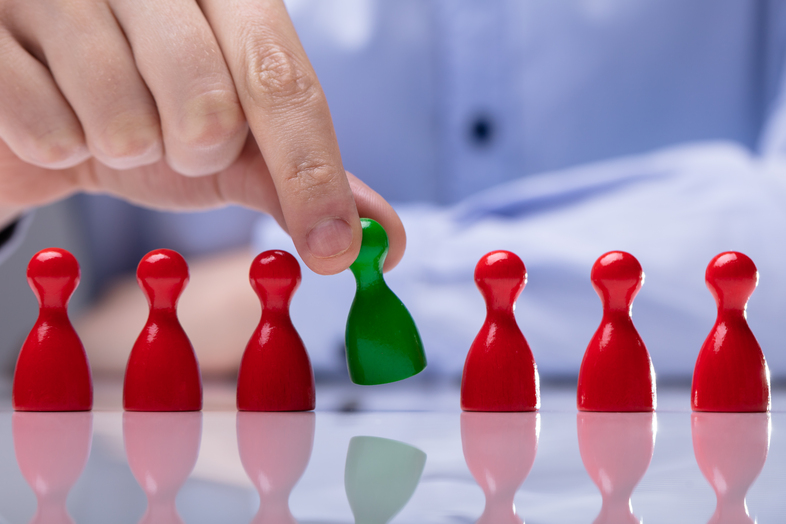 En hand lyfter en grön spelpjäs bland flera röda pjäser på ett blankt bord.
