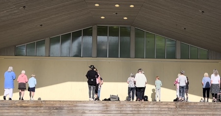 En grupp människor står utspridda på en utomhusscen med trappsteg framför.