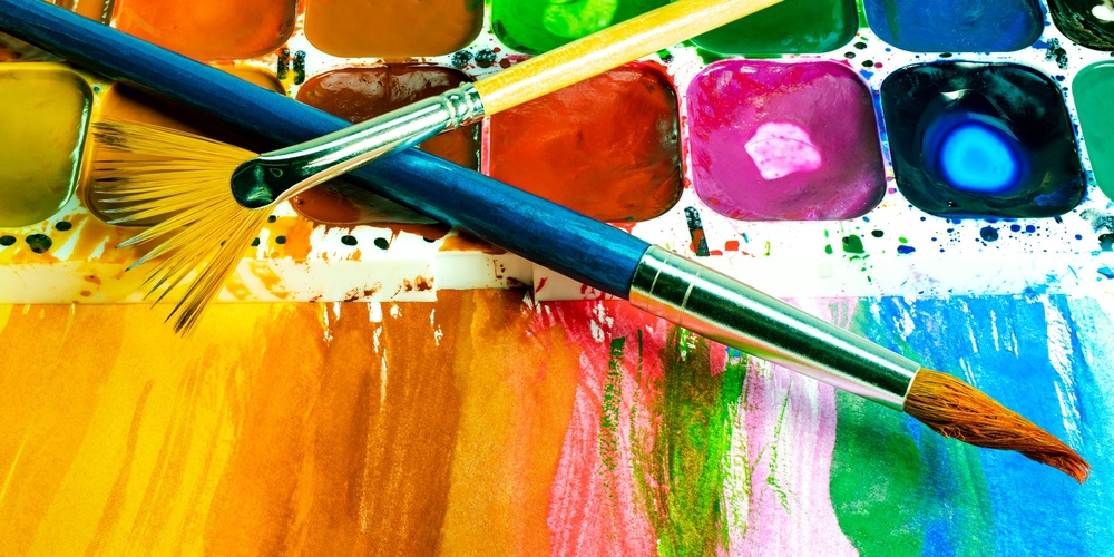 Närbild av en färgglad akvarellpalett med två penslar och målade färgfält.