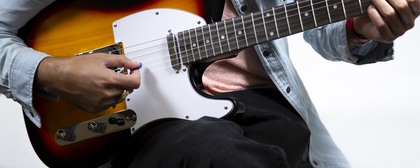 En person spelar elgitarr med en plektrum, närbild på händer och gitarr.