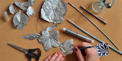 En person arbetar med metallprägling och formar blommor och blad av tunn metall på en korkmatta.