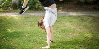 En person gör en handvolt på gräset i en grönskande park.