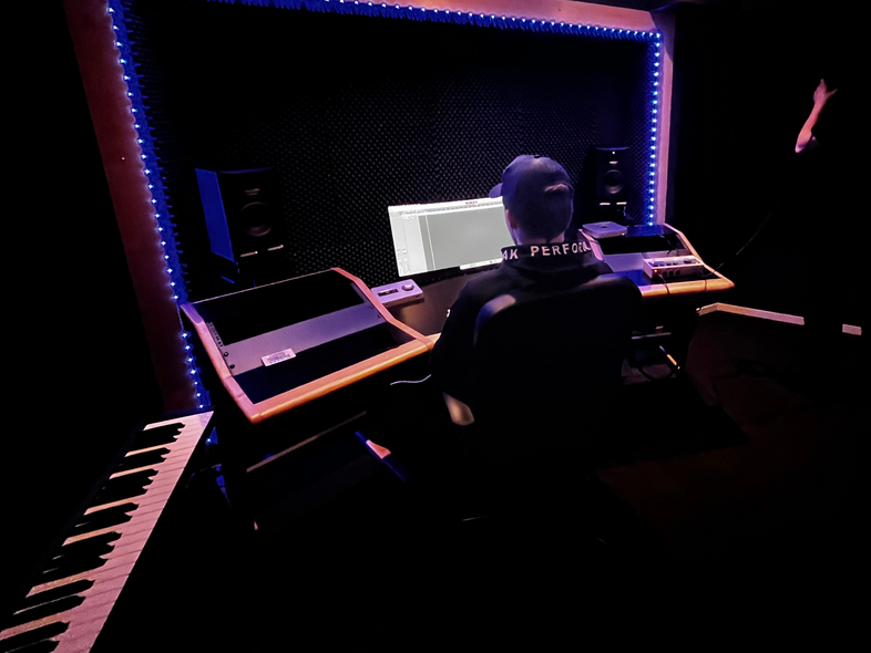 En person sitter vid ett mixerbord i en mörk inspelningsstudio med blå LED-belysning runt arbetsytan.