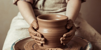 En person formar en lerkruka på en drejskiva med leriga händer.