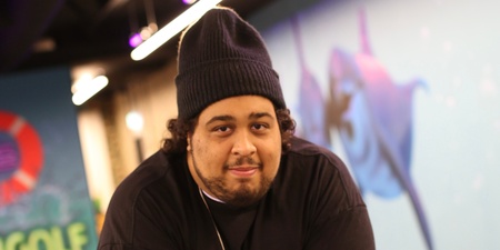 Man med mössa lutar sig mot ett bord med sprayburk och ansiktsmask i en inomhus minigolfmiljö.