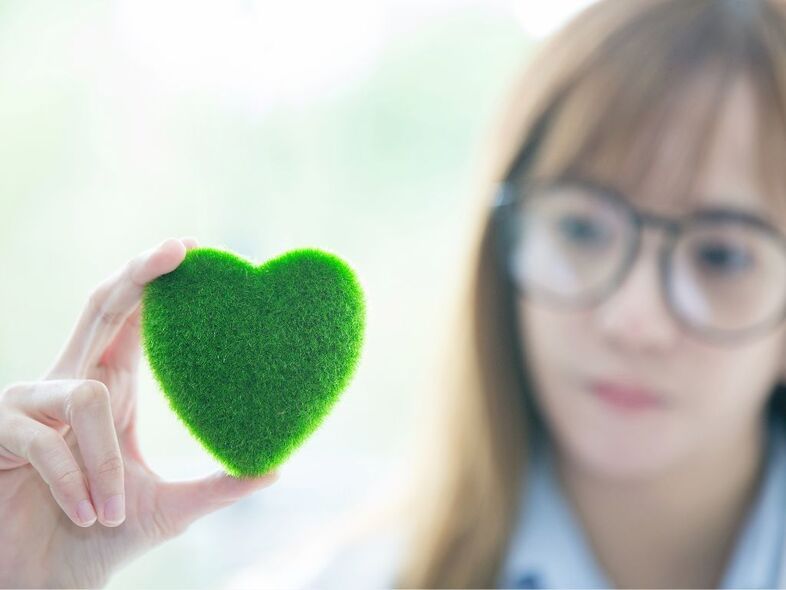 En närbild på en hand som håller upp ett grönt hjärta i filt.