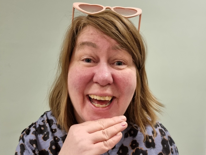 Person med axellångt hår, leopardmönstrad skjorta och rosa hjärtformade solglasögon på huvudet, håller handen mot ansiktet.