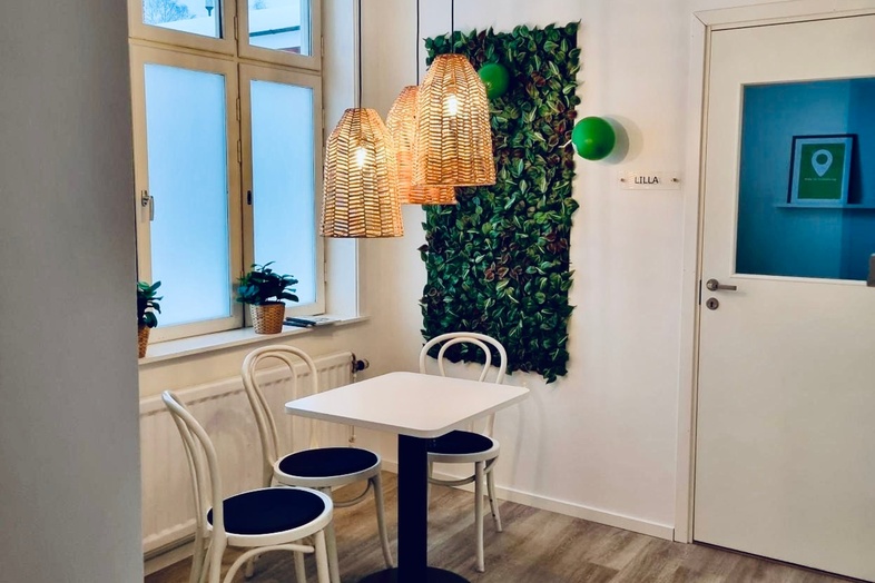 Litet matbord med två stolar, hängande lampor, växtvägg och fönster i ett ljust rum med trägolv.