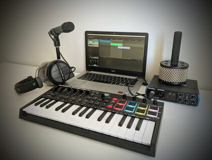 Ett hemmastudio-setup med laptop, MIDI-keyboard, mikrofon, hörlurar och ljudinterface på ett bord.