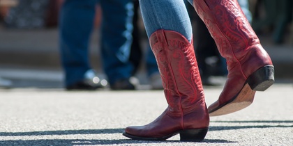 Person i blå jeans och röda cowboyboots dansar utomhus på asfalt.