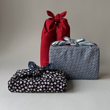 Tre paket inslagna i tyg med japansk furoshiki-teknik, i rött och blått mönstrat tyg.