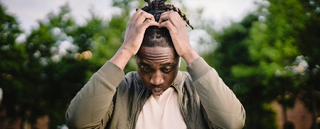 En man sitter utomhus framför en laptop och håller sig för huvudet, ser bekymrad ut.