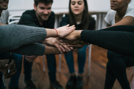 En grupp människor sitter i en cirkel och lägger sina händer ovanpå varandra i mitten som en symbol för samarbete.