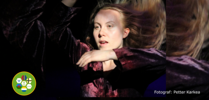 Person i lila sammetskläder dansar på scen med mörk bakgrund och färgglad logotyp i hörnet.