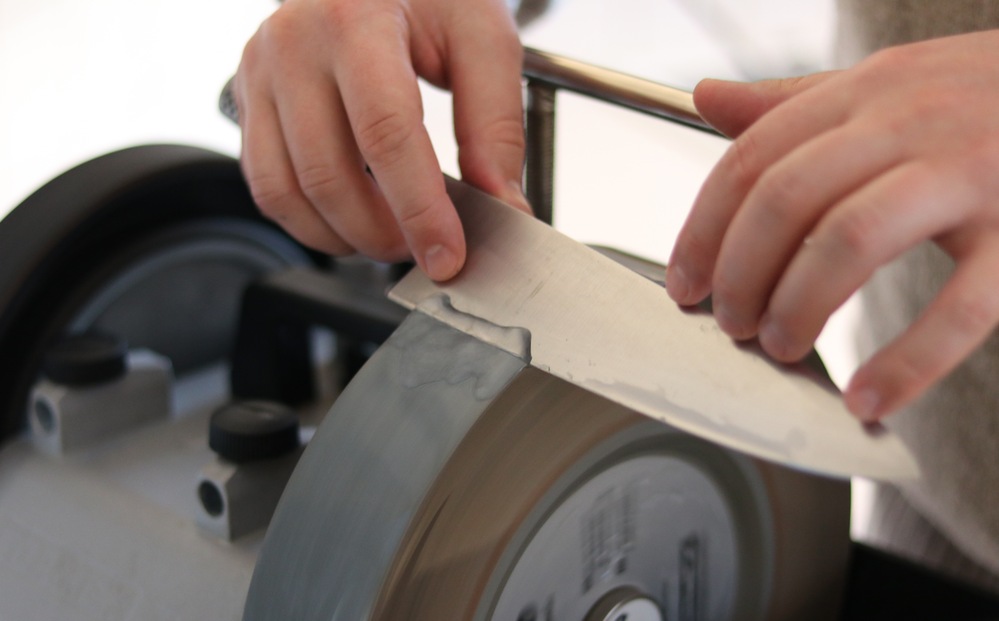 Närbild av händer som slipar en kniv mot en roterande slipsten.