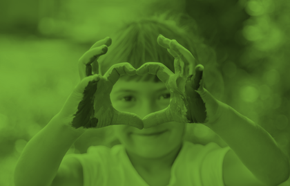 Ett barn med målade händer formar ett hjärta med fingrarna framför sitt ansikte. Bilden har ett grönt filter.