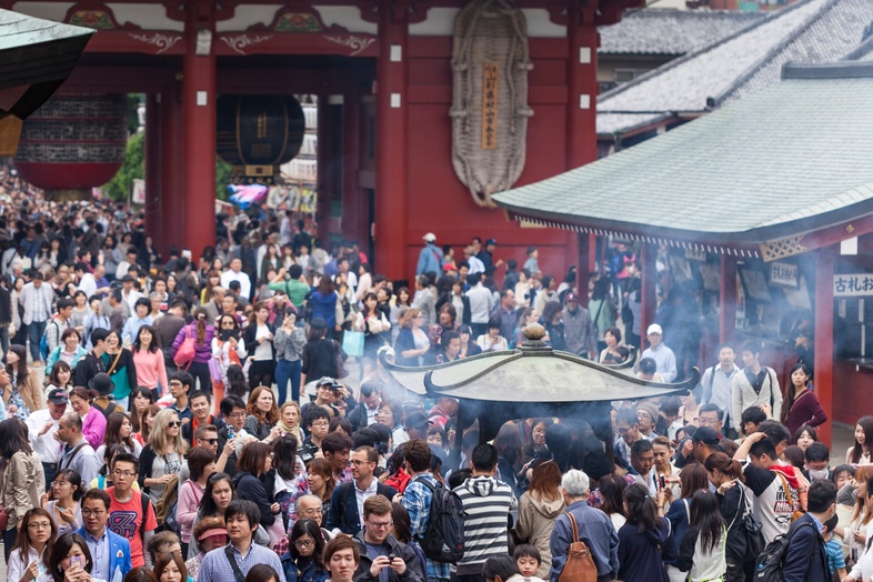 Stor folkmassa samlad vid ett tempel i Japan, med rök från en rökelsebrännare i förgrunden.