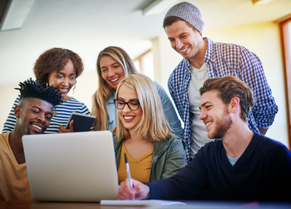 Sex unga vuxna sitter tillsammans och tittar på en bärbar dator, leende och samarbetande.