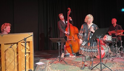 Fyra musiker uppträder på scen, med piano, kontrabas, trummor och sångerska vid mikrofon.