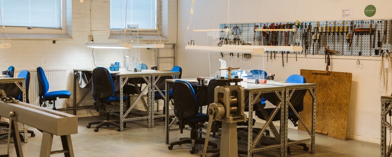 Ett ljust och modernt verkstadsrum med flera arbetsbord, stolar och verktyg på väggarna.