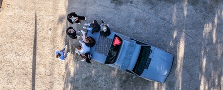 Fågelperspektiv av en grupp människor som står vid en bil på en grusväg.