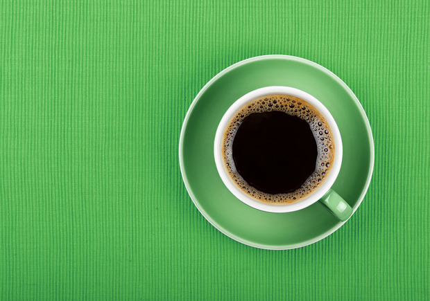 En kopp svart kaffe i en grön kopp och fat, sedd uppifrån på en grön bakgrund.