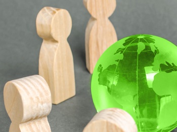 Träfigurer står i en cirkel runt en grön genomskinlig jordglob på grå bakgrund.