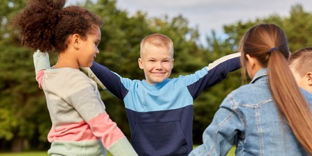 Fyra barn leker tillsammans utomhus på en gräsmatta, håller varandra i händerna.