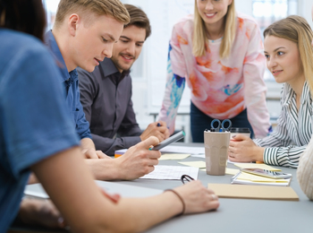 En grupp unga vuxna sitter runt ett bord och diskuterar dokument och en surfplatta.