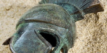 En antik hjälm av brons ligger delvis nedgrävd i sanden.