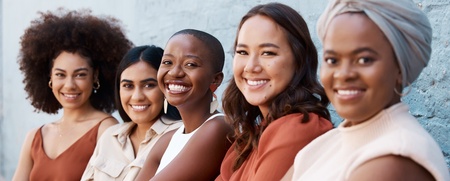 Fem kvinnor sitter i rad utomhus, ler mot kameran och ser avslappnade ut.