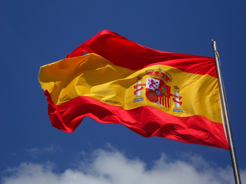 Spaniens flagga vajar mot en blå himmel med några moln.
