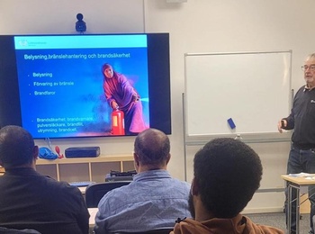 Föreläsning om brandsäkerhet i ett klassrum med deltagare och en presentatör vid en stor skärm.