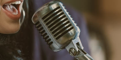 Kvinna med hörlurar sjunger i mikrofon i en studio.