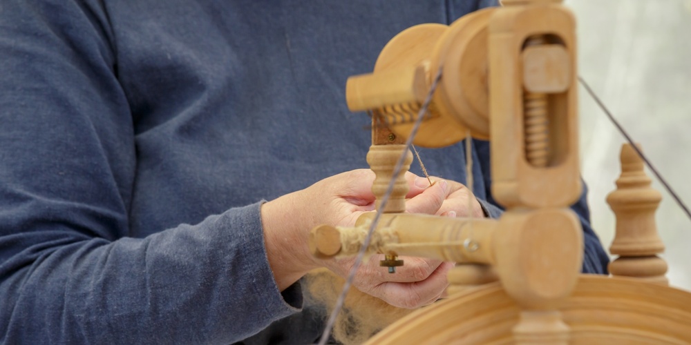 Person spinner garn med en gammaldags spinnrock, fokus på händer och verktyg.