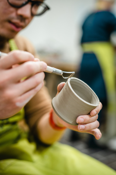 En person dekorerar en lerkruka med ett verktyg i en keramikverkstad.