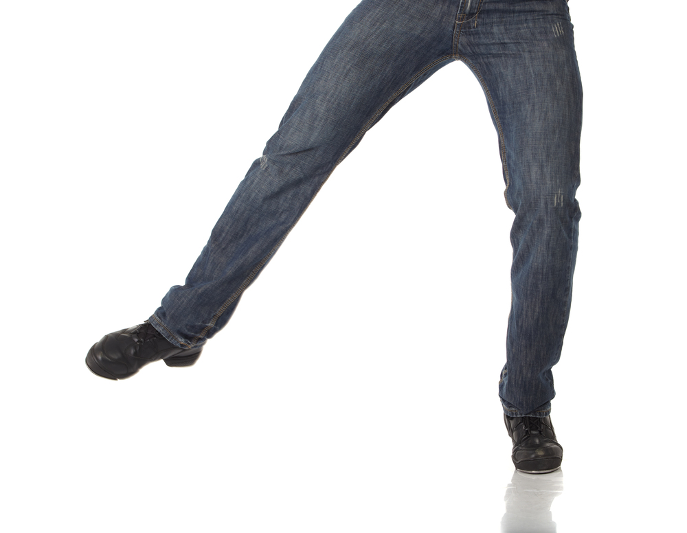 En person i blå jeans och svarta skor står med benen isär mot vit bakgrund. Överkroppen syns inte.