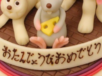 Dekorerad tårta med figurer av en kanin, en mus och en hund samt japansk text.