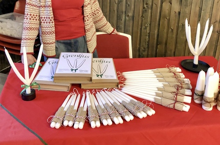 Ett bord med vita ljus, böcker och ljusstakar, samt en person i röd tröja bakom bordet.