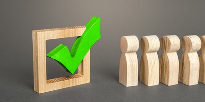 Träfigurer står bredvid en stor grön bock i en träram mot grå bakgrund.