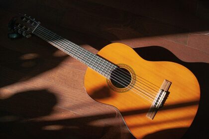 En klassisk akustisk gitarr ligger på ett trägolv med solstrålar och skuggor över instrumentet.