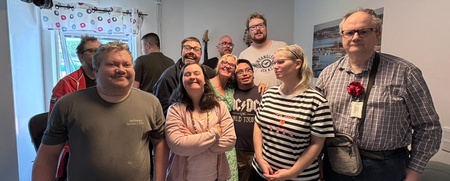 En grupp människor står tillsammans i ett rum med ljusa väggar och fönster, ansikten är suddade.