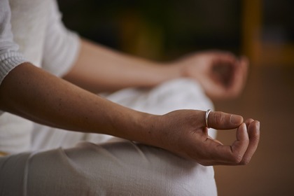 En person sitter i meditationsställning med händerna vilande på knäna, fokus på händerna.