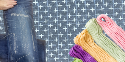 Hand lagar ett par jeans med sashiko-broderi, färgglada broderigarn syns bredvid.