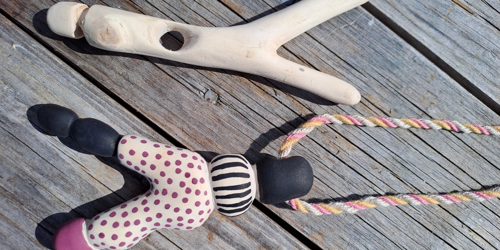 En gammaldags klädnypa i trä och en färgglad docka med snöre ligger på ett trägolv utomhus.