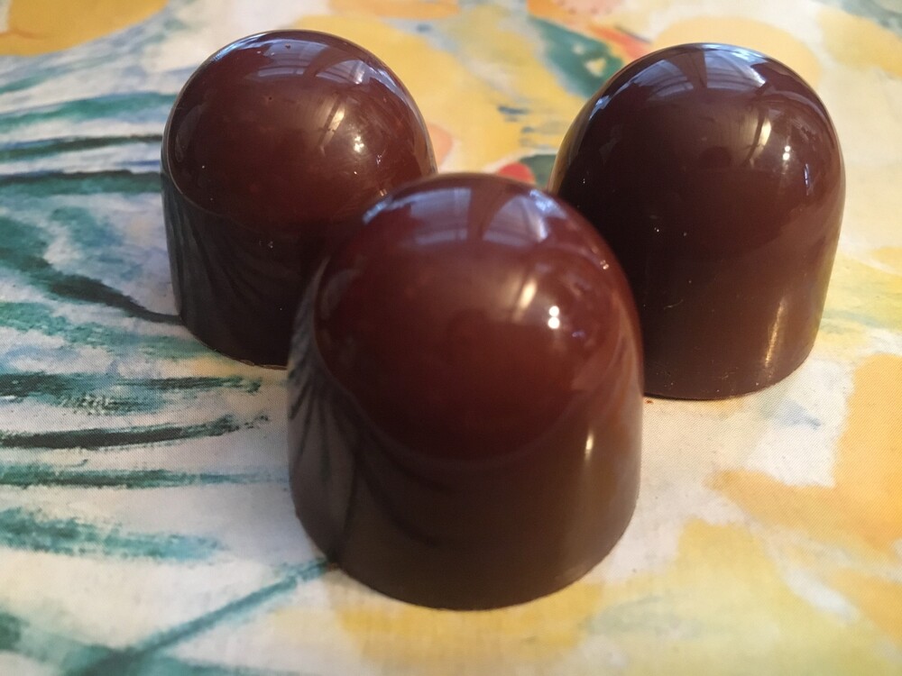 Tre blanka, mörka chokladpraliner står på ett färgglatt underlag.