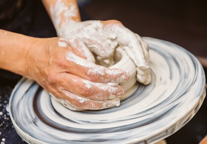 Närbild av händer som formar lera på en drejskiva under keramikarbete.