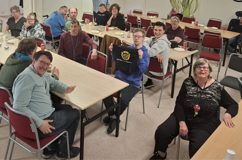 En grupp människor sitter runt bord i ett samlingsrum och fikar tillsammans.